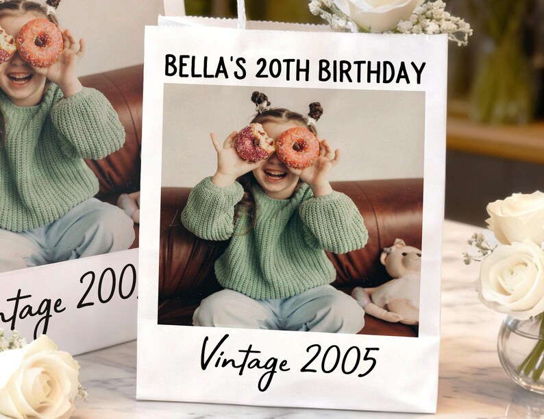 Pu&ograve; includere: Un sacchetto regalo bianco con una foto di una giovane persona che tiene delle ciambelle sugli occhi. Il sacchetto presenta la scritta "BELLA'S 20TH BIRTHDAY" e "Vintage 2005" in nero.