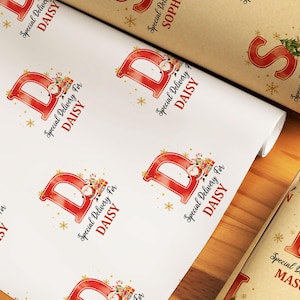 May include: White wrapping paper featuring a repeating pattern of a red letter "B" with a Santa Claus graphic and the text "Special Delivery For DAISY". A roll of brown paper with a red letter "S" and the text "Special Delivery For SOPHIA" is also visible.