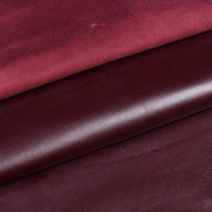 May include: Close-up of three pieces of burgundy leather. The top piece has a matte finish, while the middle and bottom pieces have a smooth, glossy appearance. The leather is a deep, rich shade of red.
