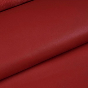 Peut inclure: Gros plan sur un morceau de cuir rouge. Le cuir a une surface lisse, légèrement texturée et une couleur riche et unie. Le matériau est plié, montrant le dessous et l'épaisseur.