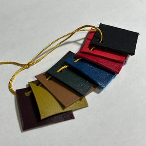 May include: A color swatch set featuring small, rectangular leather samples in various colors, including black, red, blue, and brown. The samples are attached to a gold cord, showcasing the range of available hues.