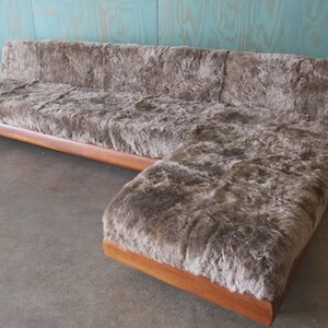 May include: A mid-century modern sectional sofa with a plush, shaggy, brown upholstery. The sofa features a wooden frame and a chaise lounge on the right side. The design is a blend of comfort and retro style.