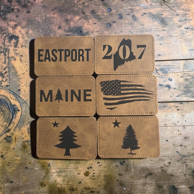 May include: Six rectangular tan faux leather patches with dark brown laser-engraved designs. The patches feature the text EASTPORT, the number 207 with a Maine state outline, the text MAINE with a tree, a distressed American flag, and two pine trees.