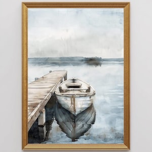 Op de afbeelding: Een ingelijste aquarelprint van een boot afgemeerd aan een houten steiger op een kalm meer. De boot is wit en het water en de lucht zijn tinten blauw en grijs. De lijst is goudkleurig.