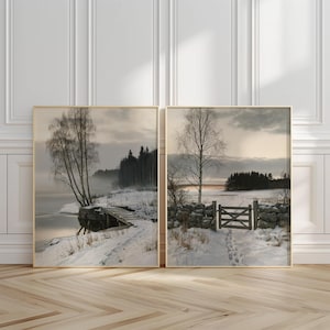 Op de afbeelding: Twee ingelijste wandkunstprints met winterlandschappen. De linkerprint toont een besneeuwde oever met een houten steiger en berkenbomen. De rechterprint toont een stenen muur met een houten hek dat leidt naar een bos in de sneeuw.