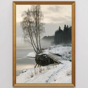 Op de afbeelding: Een ingelijste landschapsafdruk van een besneeuwde oever in de winter. De scène toont een houten steiger die in kalm water uitsteekt, hoge berkenbomen en een dicht bos onder een mistige, bewolkte lucht. Het kunstwerk zit in een gouden lijst.