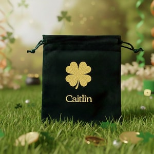 May include: A dark green velvet drawstring bag with a gold glitter shamrock and the name "Caitlin" printed on the front. The bag is set on a bed of green grass with gold coins and shamrock confetti.