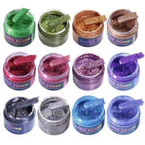 May include: Twelve round jars of glitter paste in various colors including green, bronze, red, purple, silver, and blue. Each jar features a label with the text "FABER PASTE" and contains a small spatula resting inside the thick, textured paste.