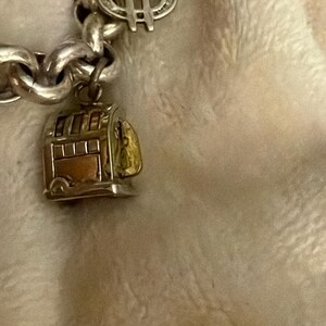 Puede incluir: Pulsera de plata con un charm de signo de d&oacute;lar y un peque&ntilde;o charm de tranv&iacute;a detallado. El charm del tranv&iacute;a tiene detalles dorados y cobrizos, a&ntilde;adiendo un toque de color a la cadena de plata. Fondo suave.