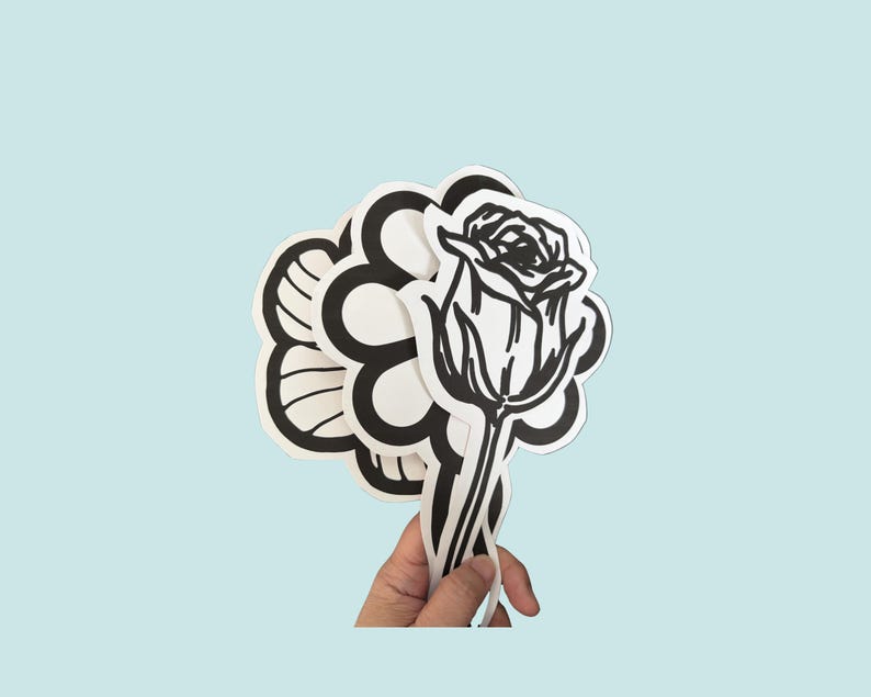 May include: A collection of die-cut stickers featuring black and white line art designs. The stickers include a detailed rose, a stylized flower with rounded petals, and other floral-inspired shapes with bold outlines and white borders.