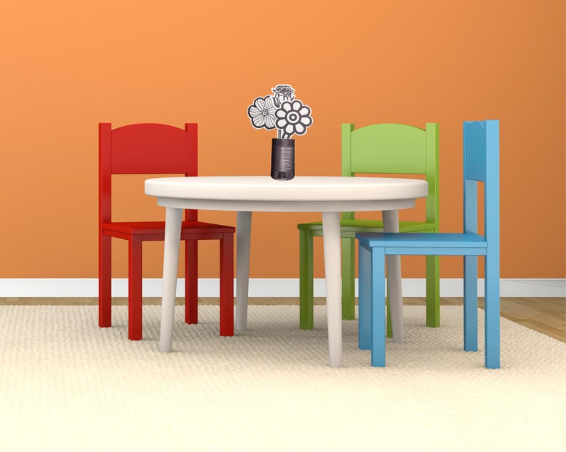 May include: A white round table with four tapered legs, accompanied by three wooden chairs in red, lime green, and blue. A small dark vase sits in the center of the table, holding a bouquet of three black and white line-art flower cutouts.
