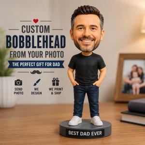 May include: A custom bobblehead figure of a man with dark hair and a beard, wearing a black t-shirt, dark blue jeans, and white sneakers. The figure stands on a circular gray base with the text BEST DAD EVER printed in white on the front.