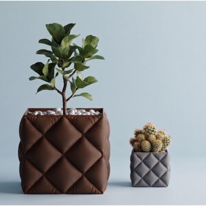May include: A large square brown planter with a quilted texture containing a green leafy plant and white pebbles, next to a smaller square grey quilted planter containing a cluster of small green cacti on a light blue background.