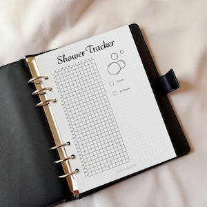 May include: A black leather binder with a shower tracker insert. The insert has a grid for tracking daily showers, with the title "Shower Tracker" in a script font. Includes bubble graphics and check boxes for "Shower" and "No Shower".