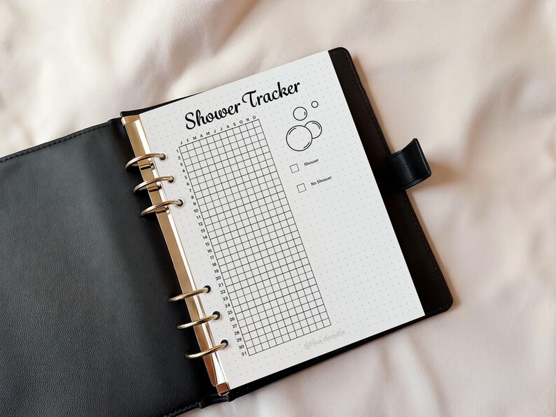 May include: A black leather binder with a shower tracker insert. The insert has a grid for tracking daily showers, with the title "Shower Tracker" in a script font. Includes bubble graphics and check boxes for "Shower" and "No Shower".