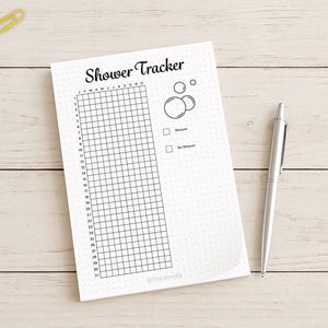 May include: A white notepad with the words "Shower Tracker" and a grid for tracking daily showers. Includes a pen and colorful paperclips. The notepad has a dotted background and a simple bubble graphic.
