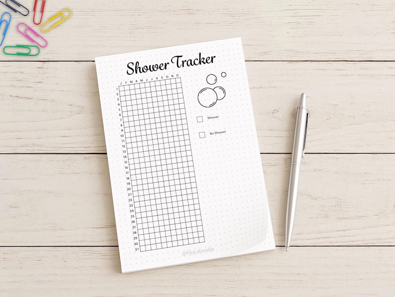 May include: A white notepad with the words "Shower Tracker" and a grid for tracking daily showers. Includes a pen and colorful paperclips. The notepad has a dotted background and a simple bubble graphic.
