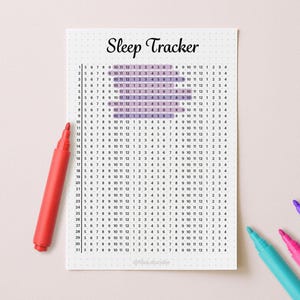 May include: A white "Sleep Tracker" printable with a grid for tracking sleep patterns. The grid is filled with numbers and highlighted sections. A red marker and three other colored markers are on the light pink surface.