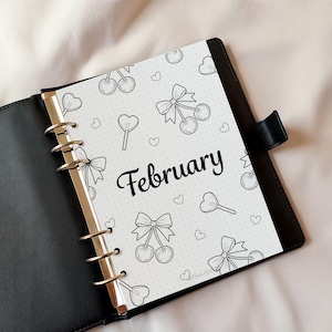 February monthly bullet journal cover page shown inside a ring binder planner. Black and white illustrated journal cover with a dotted background and seasonal heart and bow motifs. Printable monthly journal cover designed for bullet journals and planners, suitable for A4 and A5 sizes.