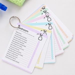 Laminated cleaning cards displayed on a binder ring for easy access and organization. Reusable room-by-room cleaning checklist cards designed for ADHD-friendly cleaning routines. Printable Canva editable cleaning cards can be laminated, checked off, wiped clean, and reused for household chores and home organization.