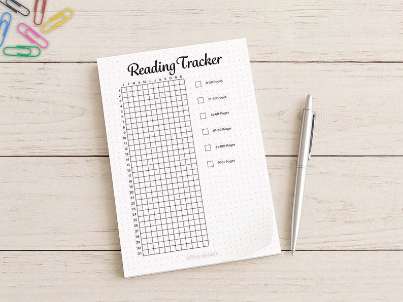 Op de afbeelding: Een witte "Reading Tracker" notitieblok met een raster om de leesvoortgang bij te houden. Het notitieblok heeft een titel en selectievakjes voor pagina-aantallen. Een zilveren pen ligt naast het notitieblok op een licht houten oppervlak.