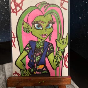 Peut inclure: Illustration dessinée à la main d'un personnage à la peau verte avec des cheveux roses et verts, portant un gilet bleu et une chemise noire avec le mot "Punk". Le personnage fait un geste de la main rock. L'œuvre est exposée sur un petit chevalet en bois.