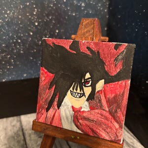 May include: A small, square painting on a miniature wooden easel. The artwork depicts a character with black hair, a white face, and a red cloak. The character has a sinister grin and red eyes. The background is red and black.