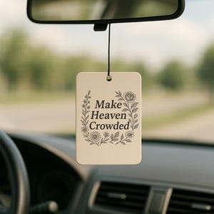 May include: A rectangular car air freshener with the text "Make Heaven Crowded" surrounded by floral illustrations. The air freshener hangs from a rearview mirror inside a car.
