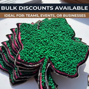 May include: A stack of green shamrock patches with pink and black trim. The patches have a textured appearance and are likely embroidered. The text "BULK DISCOUNTS AVAILABLE" is visible at the top of the image.