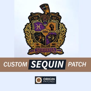 May include: A custom sequin patch with a shield design. The patch features gold, purple, and black colors with intricate details, including a tiger, a woman's bust, and the text "SHERENA". The patch also includes the text "CUSTOM SEQUIN PATCH".