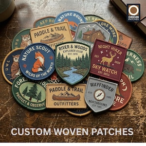 May include: A collection of embroidered fabric patches in various shapes and colors, featuring outdoor-themed designs like foxes, owls, deer, mountains, rivers, and canoes, with text including Paddle & Trail, River & Woods, and Night Hiker.