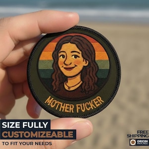 May include: A circular patch with a cartoon illustration of a woman with brown hair and a necklace, set against a sunset-colored background. The text "MOTHER FUCKER" is below the image. The patch is held in a hand.