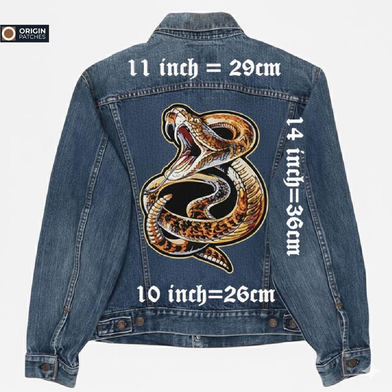 Pode incluir: Casaco de ganga azul com um grande patch bordado de uma cobra nas costas. A cobra &eacute; em tons de castanho, bege e preto. O patch mede 29 cm x 36 cm. O texto "11 inch = 29cm" e "14 inch=36cm" &eacute; vis&iacute;vel.