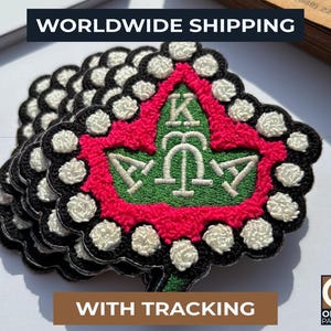 May include: A stack of embroidered patches with a green, red, black, and white design. The patches feature a central emblem with Greek letters and a leaf shape. The text "WORLDWIDE SHIPPING" is at the top.