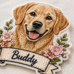 May include: An embroidered patch featuring a golden-colored dog with a smiling expression, surrounded by pink flowers and green leaves. A beige banner at the bottom displays the name Buddy in black cursive script, all outlined in white thread.