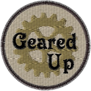 Puede incluir: Un parche redondo bordado de color beige y marrón con un diseño de engranaje y el texto "Geared Up" en negro.