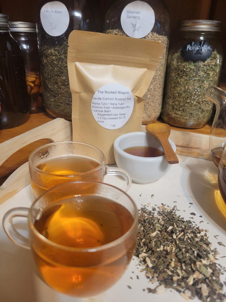 Puede incluir: Una presentaci&oacute;n de t&eacute; de hierbas. Dos tazas de vidrio transparente llenas de t&eacute; color &aacute;mbar est&aacute;n en primer plano. Un peque&ntilde;o cuenco blanco y una cuchara de madera est&aacute;n cerca. Tambi&eacute;n se ve una bolsa de papel marr&oacute;n y frascos de hierbas.