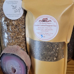 May include: A package of "Gentle Cortisol Support Tea" from The Rooted Wagon Family Apothecary, with ingredients like Rama Tulsi and Lemon Balm. The package is tan with a clear window, showing the tea inside. A sliced geode with pink and purple hues is in the foreground.