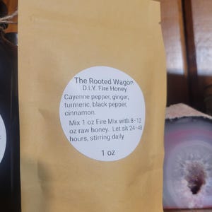 May include: A tan paper packet labeled "The Rooted Wagon D.I.Y. Fire Honey" with a white circular label listing ingredients: cayenne pepper, ginger, turmeric, black pepper, and cinnamon. Instructions are also included. The packet is 1 oz.