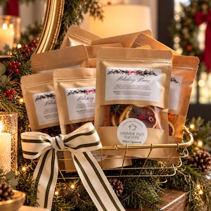 May include: A gold wire basket filled with multiple brown paper pouches of simmer potpourri. Each pouch features a label reading Holiday Home and Simmer Pot Shoppe, with a clear window revealing dried orange slices, cranberries, and rosemary sprigs.
