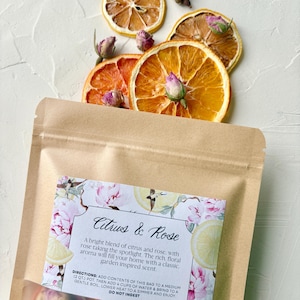 May include: A kraft paper bag labelled "Citrus & Rose" is displayed with dried orange and lemon slices, and small pink rose buds. The label describes a blend of citrus and rose with a garden-inspired scent.