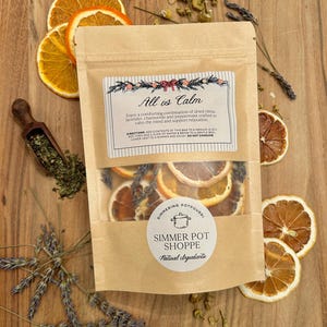 May include: A brown paper bag of simmer potpourri with dried orange slices, lavender, and chamomile. The label reads "All is Calm" and "Simmer Pot Shoppe". The ingredients are visible through a clear window.