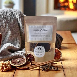 May include: A brown paper bag labelled "Scents of Autumn" with dried orange slices, cinnamon sticks, and star anise. The bag has a clear window showing the contents. A "Simmer Pot Shoppe" sticker is on the bag.