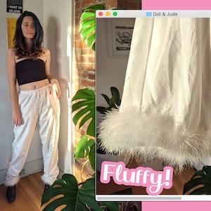 May include: White satin pants with a fluffy white feather trim at the bottom of the legs. The pants have a drawstring waist and are styled with a black bandeau top.
