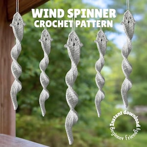 Può includere: Diversi wind spinner all'uncinetto bianchi sono appesi. Ogni spinner ha una testa a forma di pesce e un corpo a spirale. Il testo "WIND SPINNER CROCHET PATTERN" è visualizzato sopra.