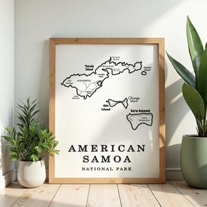 May include: A framed print featuring a black and white map of American Samoa, with island names and the text "AMERICAN SAMOA NATIONAL PARK" in a bold font. The map is set against a white background within a light wood frame.
