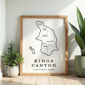May include: A framed print featuring a black and white map of Kings Canyon National Park. The map highlights locations like Mist Falls and Simpson Meadow. The text "KINGS CANYON NATIONAL PARK" is displayed below the map in a bold font. The frame is made of light brown wood.
