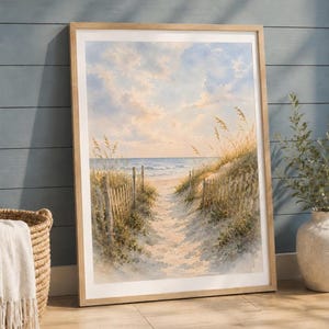 May include: A framed watercolor painting depicting a sandy beach path leading to the ocean. The scene features tall golden beach grass, a weathered wooden fence lining the path, and a soft blue sky with light clouds illuminated by sunlight.
