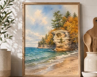 May include: A framed landscape painting depicting a rocky cliff formation extending into blue water. The scene features a sandy shoreline, evergreen and autumn-colored trees atop the cliff, and a bright blue sky with white clouds.