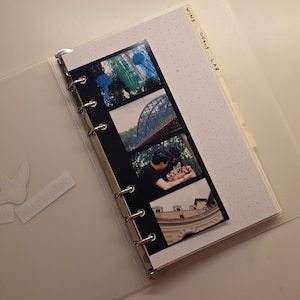 May include: A clear, plastic binder with a photo strip of four images. The photo strip is attached to a dotted paper page. The words "WINS GOALS LAB" are written on a tab. A white sticker is on the binder.